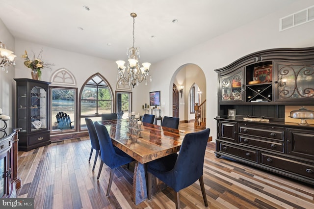 dining space featuring visible vents, arched walkways, an inviting chandelier, and wood finished floors