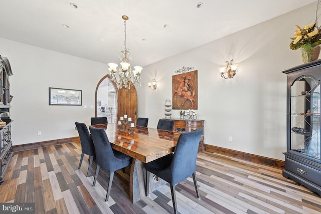 dining area featuring arched walkways, a notable chandelier, baseboards, and wood finished floors