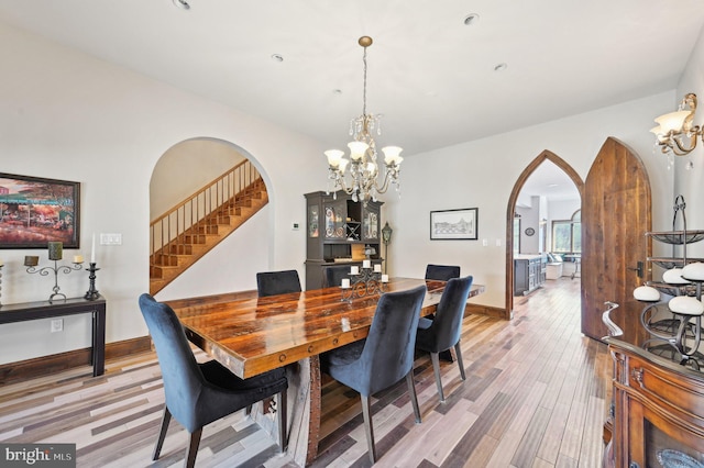 dining room featuring light wood finished floors, baseboards, a chandelier, stairs, and arched walkways