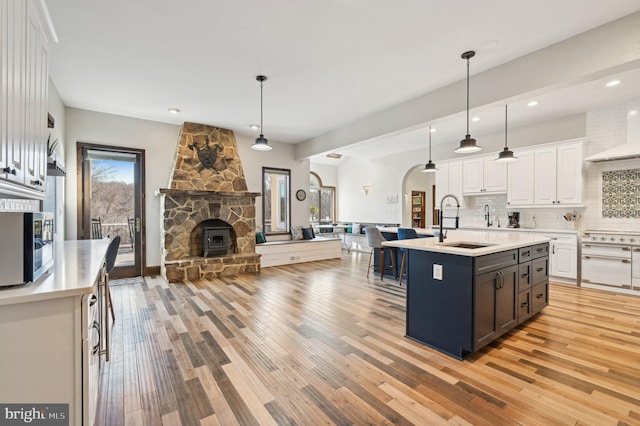 kitchen with a sink, stainless steel microwave, white cabinetry, arched walkways, and decorative backsplash