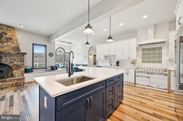 kitchen with arched walkways, a sink, decorative backsplash, white cabinetry, and wall chimney range hood