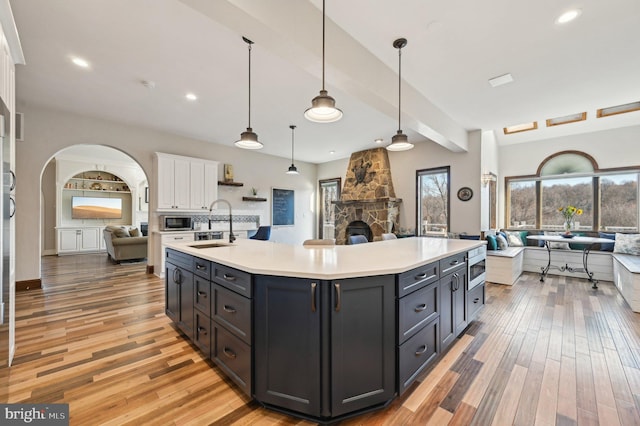 kitchen with a sink, light countertops, white cabinets, stainless steel microwave, and open floor plan