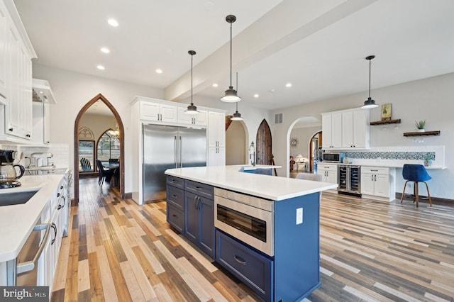 kitchen featuring wine cooler, built in appliances, arched walkways, white cabinetry, and open shelves