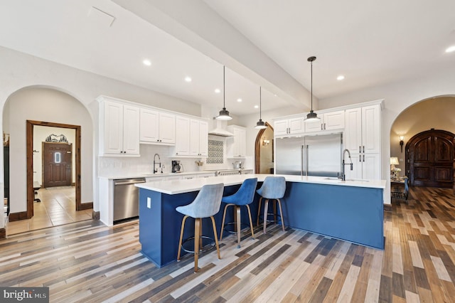 kitchen featuring arched walkways, stainless steel appliances, light wood-style floors, and a sink