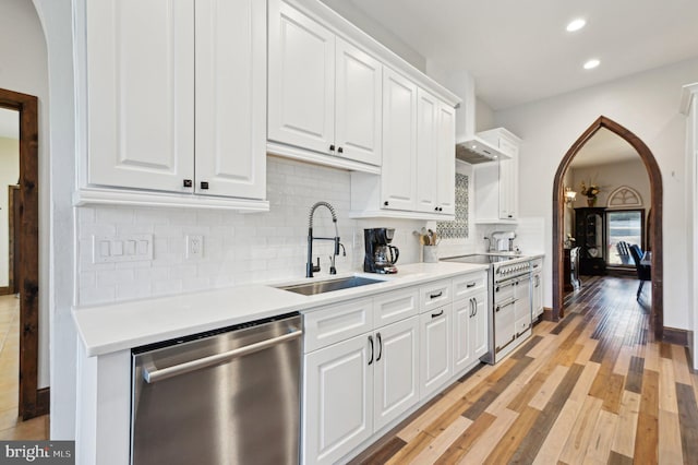 kitchen featuring light wood-style flooring, arched walkways, a sink, white cabinets, and dishwasher