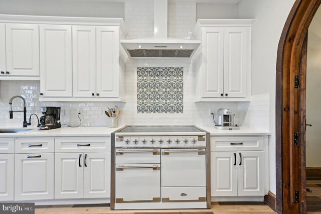 kitchen with a sink, double oven range, wall chimney exhaust hood, white cabinets, and light countertops