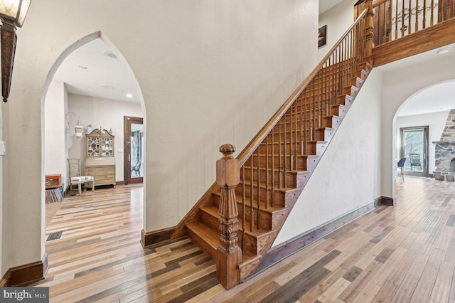 staircase with arched walkways, a towering ceiling, and hardwood / wood-style flooring