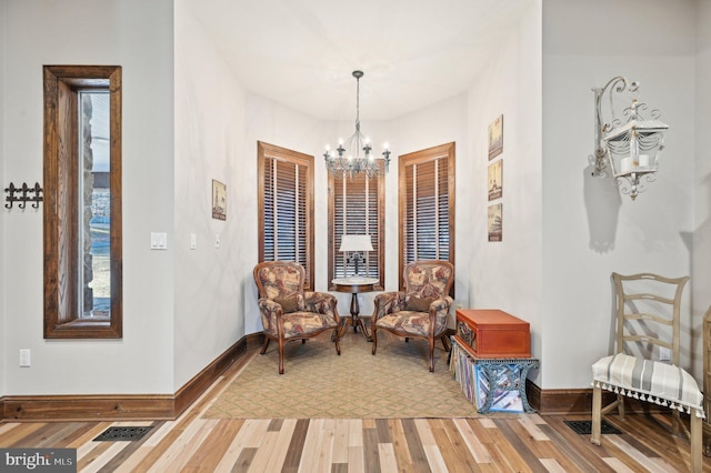 living area featuring a notable chandelier, visible vents, baseboards, and wood finished floors