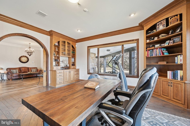 office area with visible vents, light wood finished floors, an inviting chandelier, arched walkways, and ornamental molding