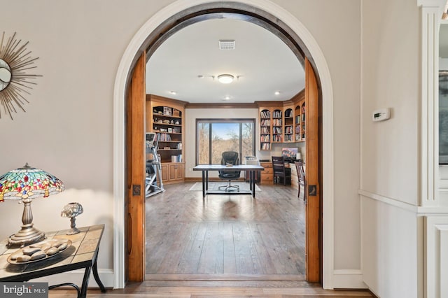 office space with arched walkways, visible vents, baseboards, and wood-type flooring