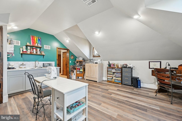 office area with vaulted ceiling, visible vents, light wood-style flooring, and a sink