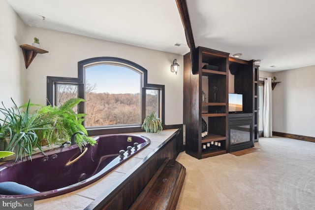 full bath featuring baseboards, a jetted tub, and a glass covered fireplace