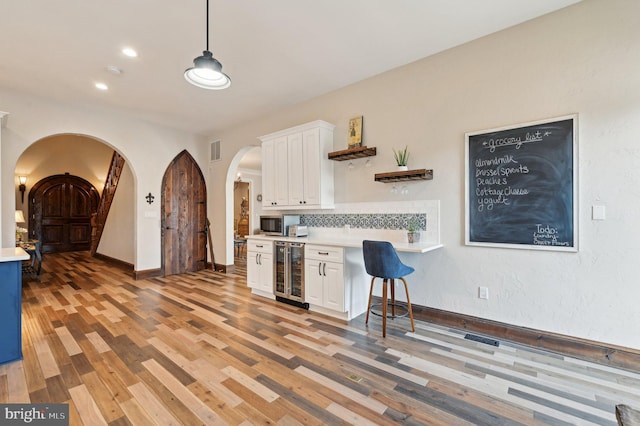 kitchen with beverage cooler, arched walkways, white cabinets, light wood finished floors, and light countertops