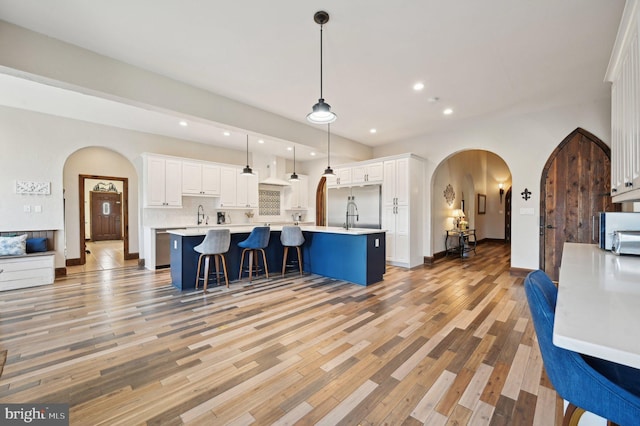 kitchen featuring arched walkways, white cabinetry, light wood-style flooring, and light countertops