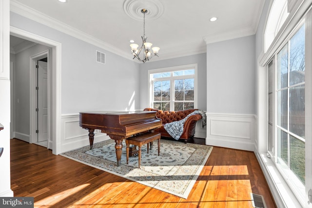 living area featuring crown molding, wood finished floors, visible vents, and an inviting chandelier