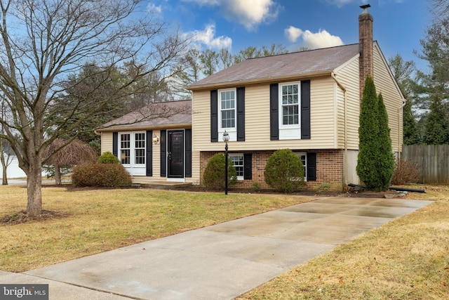 split level home with a front yard, brick siding, fence, and a chimney