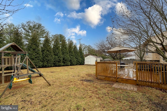 view of yard featuring a playground, an outdoor structure, fence, a wooden deck, and a shed