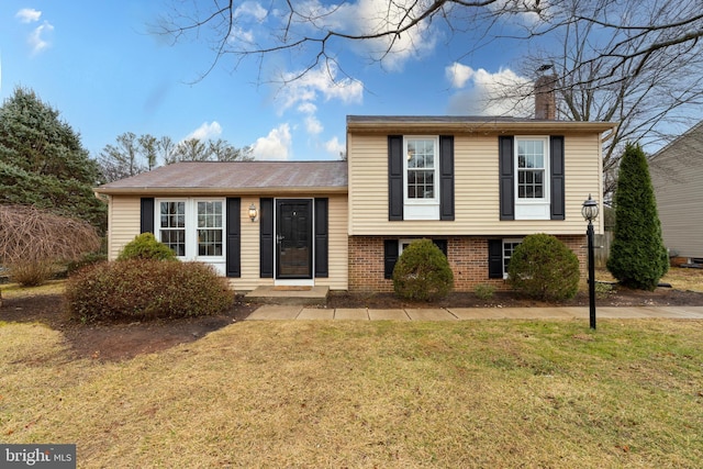 split level home with brick siding, a front lawn, and a chimney