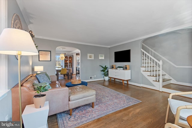 living room featuring arched walkways, dark wood-style flooring, baseboards, stairway, and crown molding