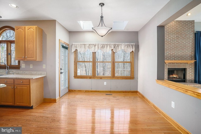 kitchen with a brick fireplace, light wood-style flooring, a skylight, and baseboards