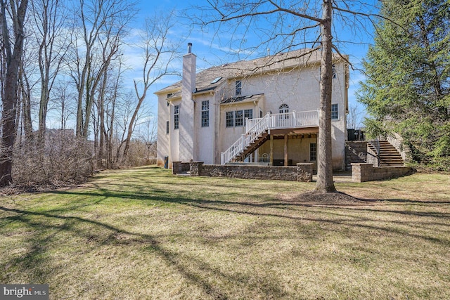 rear view of house with stucco siding, a yard, a chimney, and stairs