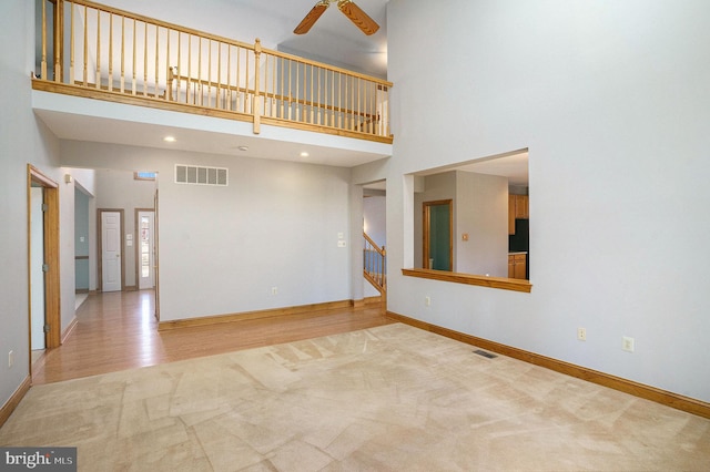 unfurnished living room featuring visible vents, baseboards, a towering ceiling, and a ceiling fan