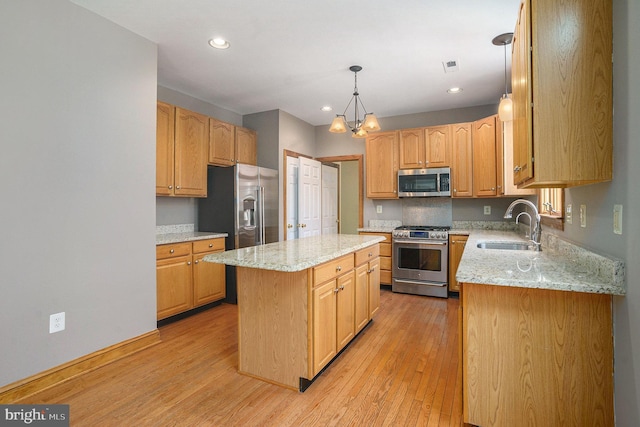 kitchen featuring light wood-style flooring, a sink, a center island, stainless steel appliances, and light stone countertops