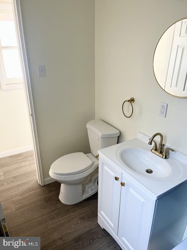 bathroom with toilet, wood finished floors, vanity, and baseboards