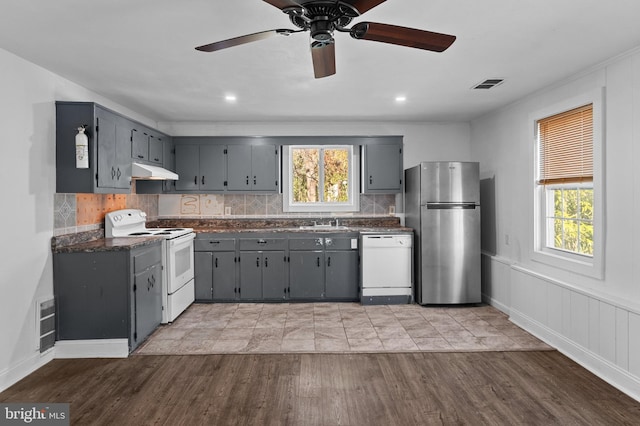 kitchen featuring gray cabinets, dark countertops, white appliances, and under cabinet range hood