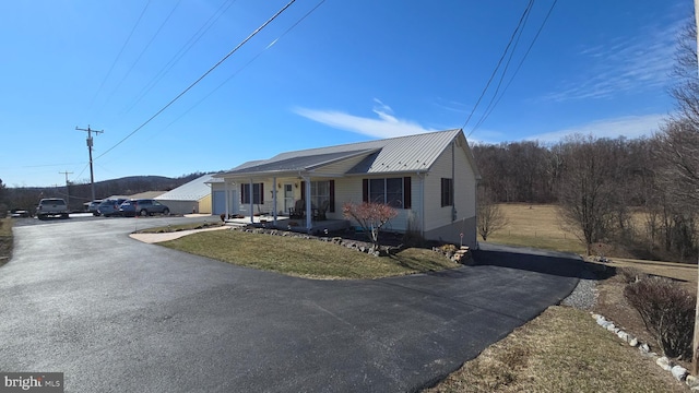 view of front of property with covered porch, metal roof, aphalt driveway, and a front yard