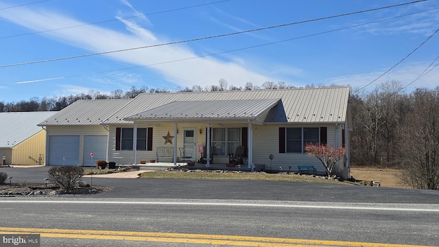 view of front facade with an attached garage, metal roof, a porch, and aphalt driveway