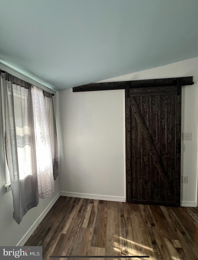 unfurnished room with lofted ceiling, dark wood-type flooring, a barn door, and baseboards