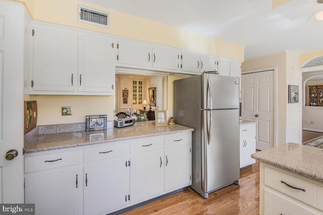 kitchen featuring visible vents, white cabinetry, freestanding refrigerator, light stone countertops, and light wood finished floors