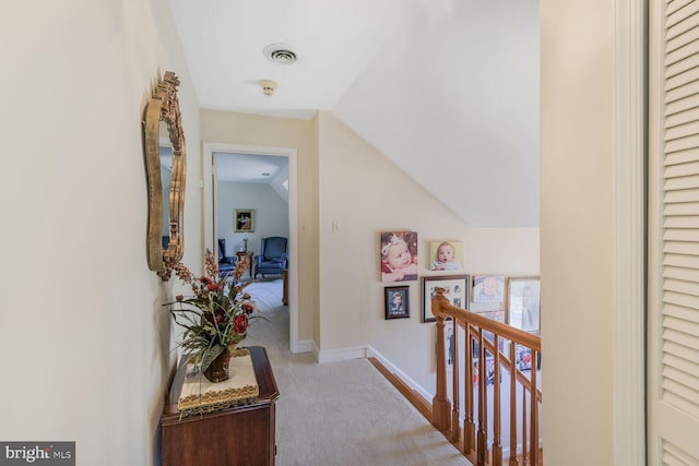 hallway with carpet, visible vents, vaulted ceiling, an upstairs landing, and baseboards