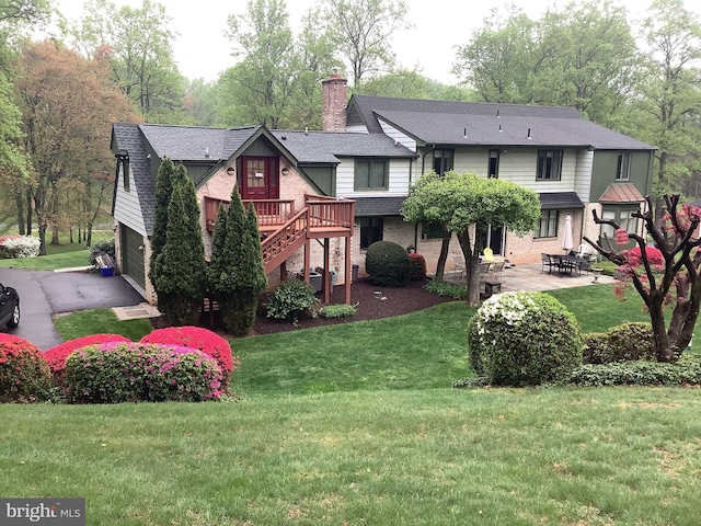 back of property with a patio, an attached garage, brick siding, a lawn, and a chimney