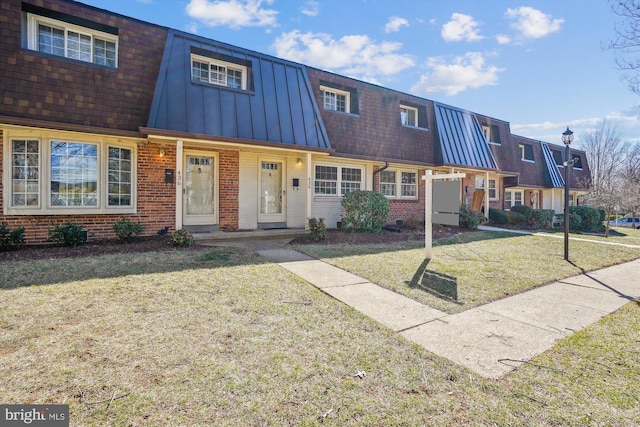 view of front of property with metal roof, mansard roof, brick siding, a standing seam roof, and a front yard