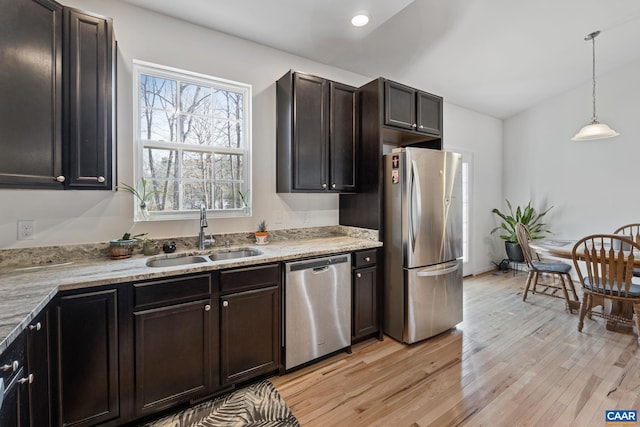 kitchen with light stone counters, stainless steel appliances, a sink, hanging light fixtures, and light wood finished floors