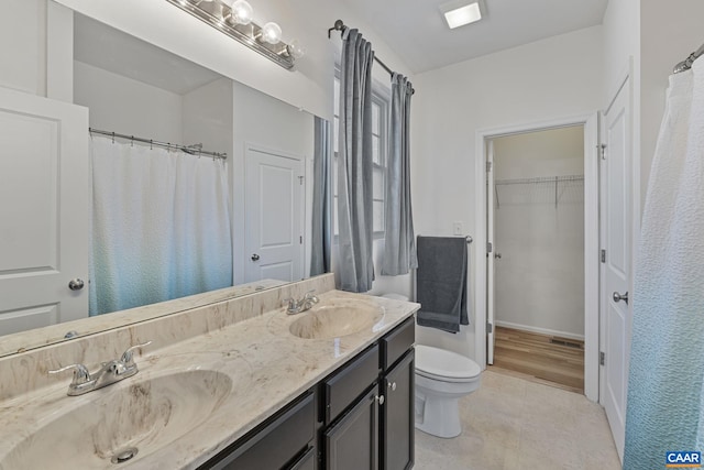 bathroom featuring a walk in closet, a sink, toilet, and double vanity