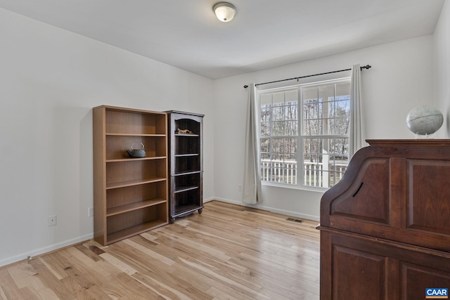 home office with light wood finished floors, visible vents, and baseboards