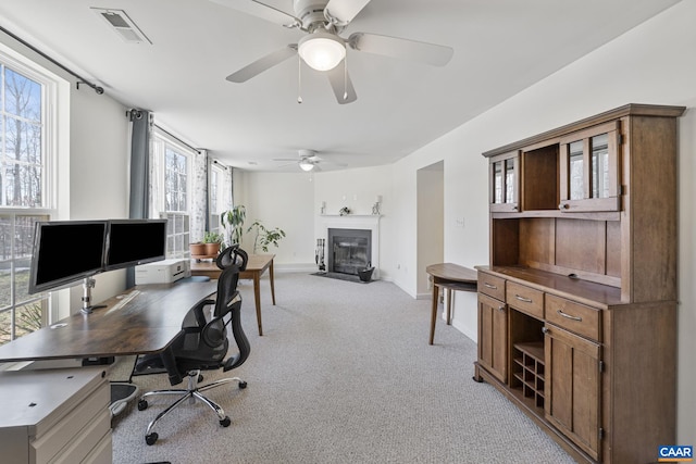 office space featuring a fireplace with flush hearth, visible vents, baseboards, and light colored carpet