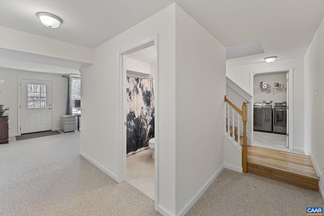 hall with baseboards, stairway, light colored carpet, and washing machine and clothes dryer