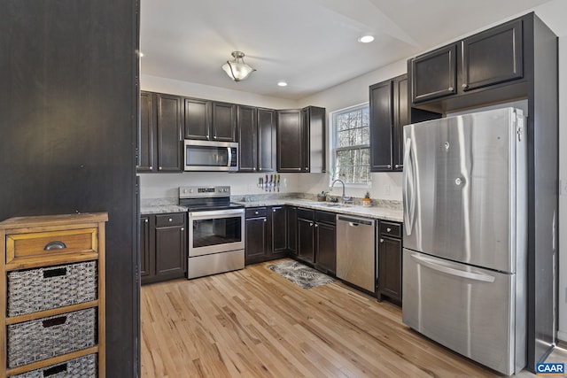 kitchen featuring light stone counters, recessed lighting, a sink, appliances with stainless steel finishes, and light wood-type flooring