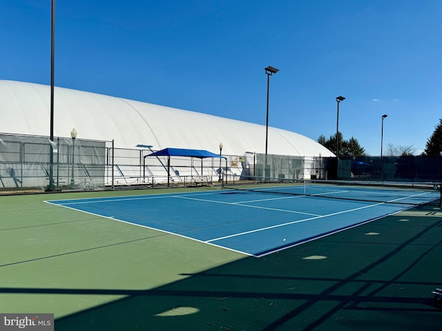 view of tennis court with community basketball court and fence