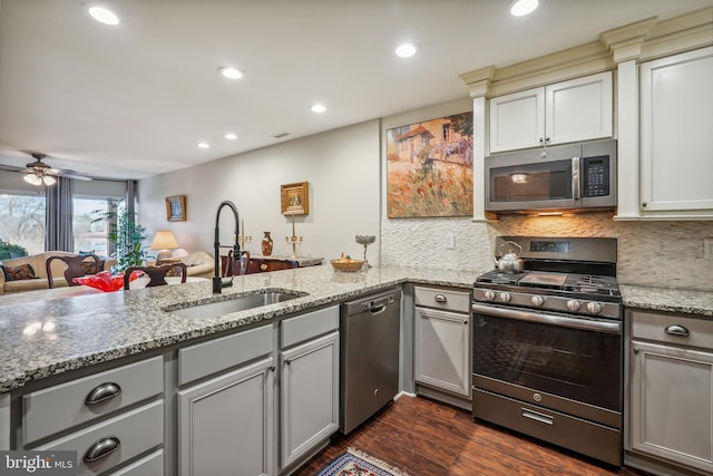 kitchen with dark wood-style floors, open floor plan, a peninsula, stainless steel appliances, and a sink