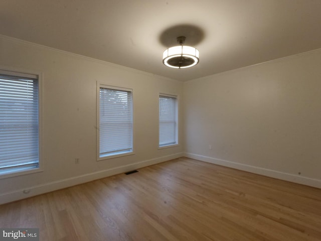 empty room featuring baseboards, light wood-type flooring, visible vents, and crown molding