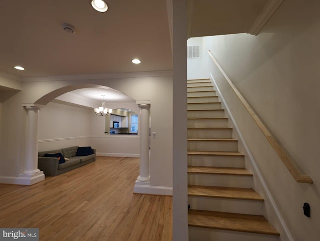 stairs with decorative columns, crown molding, arched walkways, and wood finished floors