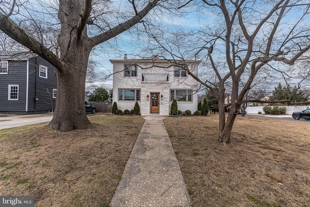 traditional home with a balcony, stone siding, and a front lawn