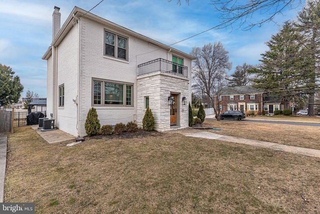 view of front of home with a front yard, a chimney, brick siding, and a balcony