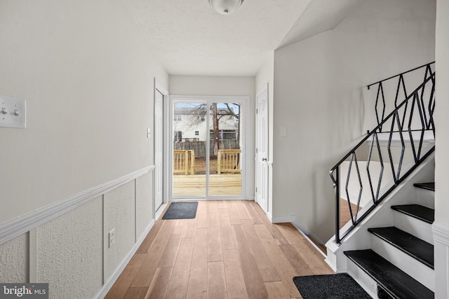 foyer with a textured ceiling, stairway, light wood-style flooring, and a wainscoted wall