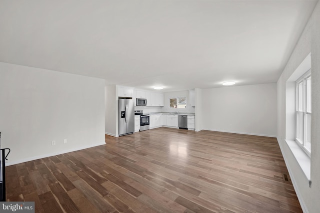 unfurnished living room with visible vents, plenty of natural light, baseboards, and wood finished floors